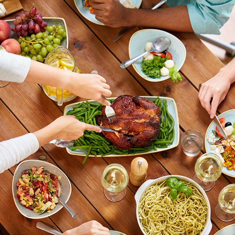 thanksgiving day, eating and leisure concept - group of people having roast chicken or turkey for dinner at table with food