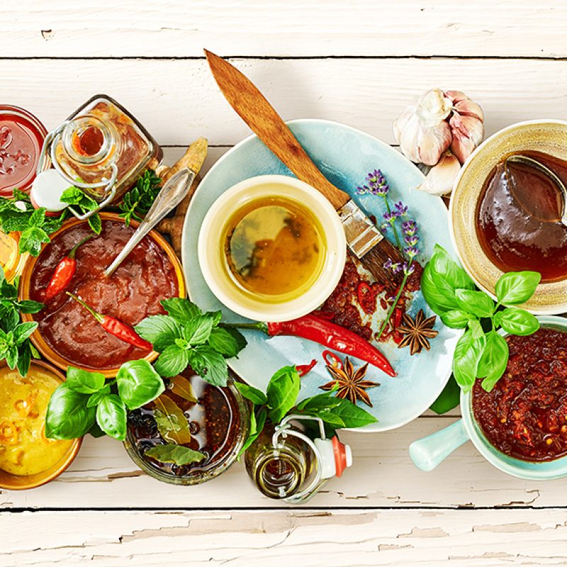 Food still life of summer marinades and sauces for a BBQ with fresh basil and spices on a rustic peeling painted white table viewed from above